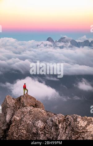 Einsamer Mann steht auf einem Bergrücken, im Hintergrund ein Wolkenmeer rund um die Agner Bergkette, Pale di San Martino Gruppe, Blick vom Costabella-Grat, Dolomiten, Italien Stockfoto