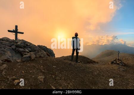 Ein Wanderer übersteht einen wolkigen Sonnenuntergang vom Gipfel der Cima Campagnaccia, Costabella Ridge, Marmolada-Gruppe, Dolomiten, Moena, Fassatal, Trient Provinz, Trentino-Südtirol, Italien. Stockfoto