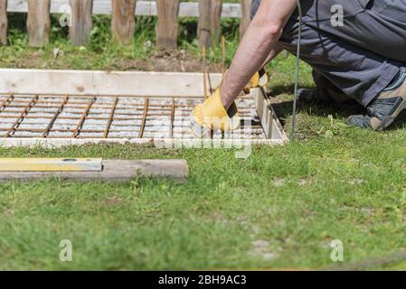 Niedrige Winkelansicht des Menschen, der ein Netz aus Stahlstangen als Verstärkung in einem Loch für ein Betonfundament draußen im Hinterhof macht. Stockfoto