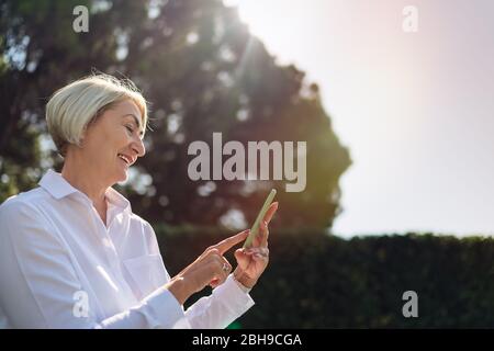 Reife Frau mit auf dem Handy während der Ruhe im Park Stockfoto