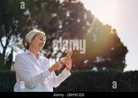 Reife Frau mit auf dem Handy während der Ruhe im Park Stockfoto
