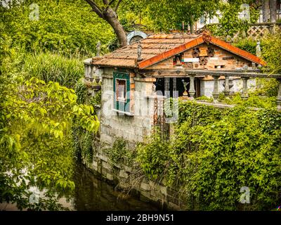 Kleines Haus am Ufer eines Baches umgeben von grüner und üppiger Natur. Statuetten und Töpferwaren schmücken das Äußere. Mantua, Lombardei, Italien. Stockfoto