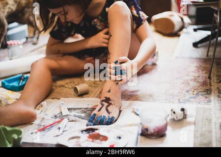 Junges Mädchen zu Hause spielen und malen ihren Fuß und ihre Hand. Stockfoto