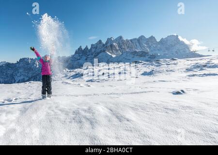 9-jähriges Mädchen spielt in der Laresei Hütte, vor der Pale di San Martino, Falcade, Dolomiten, Belluno, Venetien, Italien, Schnee in die Luft werfen Stockfoto