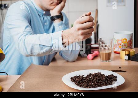 Mann gelangweilt in der Isolierung des Hauses, Zählen von Kaffeebohnen Stockfoto