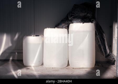 Drei gefüllte weiße Kanister unterschiedlicher Größe stehen in einer Werkstatt an einer Wand Stockfoto