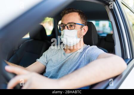 Porträt des Mannes trägt chirurgische Maske während der Fahrt ein Auto. Stockfoto
