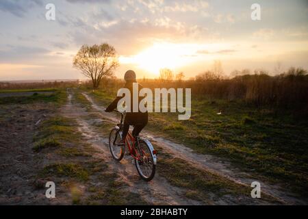 Mädchen in Jacke und Kappe Fahrrad fahren in ländlichen Feld Straße in susnet Stockfoto