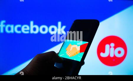 Jaipur, Indien, um 2020 - Foto eines Mobiltelefones mit einem Handschlag, was einen Deal bedeutet, mit facebook und Reliance jio im Hintergrund Stockfoto
