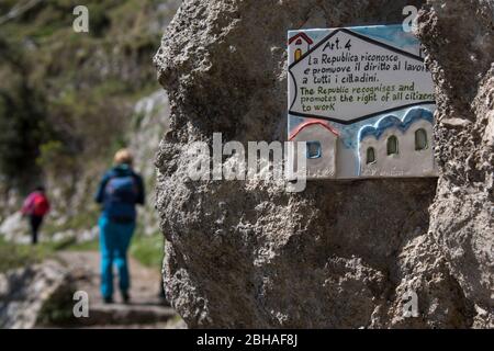 Der Weg der Götter: Sentiero degli Dei. Unglaublich schöner Wanderweg hoch über der Amalfitana oder Amalfi Küste in Italien, von Agerola nach Positano. März 2019. "Recht aller Bürger auf Arbeit": mit Botschaft unterschreiben. 2 Wanderer, Rückansicht Stockfoto