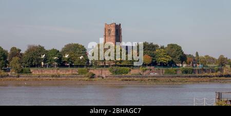 St Mary's Church und ein Schwäneflug in Widnes, der über die Mersey-Mündung von der Mersey-Fähre auf einer Kreuzfahrt entlang des Manchester Ship Canal gesehen wird Stockfoto