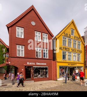 Touristen spazieren vor der Kulisse von bunten Holzhäusern mit Modehäusern im Hanseviertel in Bryggen, Torget, der Deutschen Werft, Bergen, Hordaland, Norwegen, Skandinavien, Europa Stockfoto