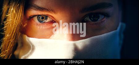 Augen einer Frau in einer Gaze-Maske, die die Kamera aus nächster Nähe anschaut. Vorbeugender Schutz Ihrer eigenen Gesundheit vor Virusinfektionen. Coronavirus-Konzept. Stockfoto