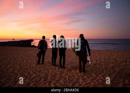 Vier Surfer stehen am Strand bei Sonnenuntergang, Huntington Beach, Kalifornien, USA Stockfoto