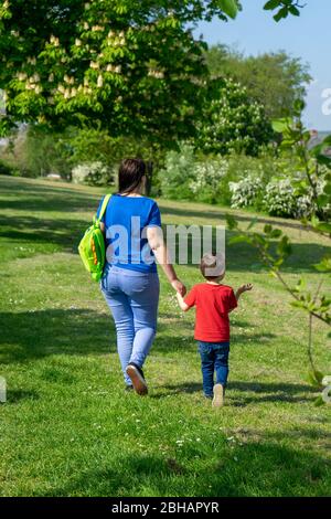 Eine Mutter und ein Sohn gehen im Frühling mit den Händen nach draußen Stockfoto