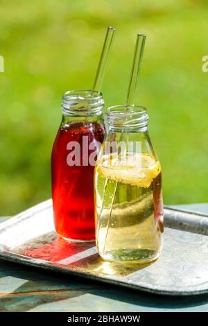 Zwei kleine Glasflaschen mit selbstgemachter Zitrone und Holunderlemonade auf einem Gartentisch Stockfoto