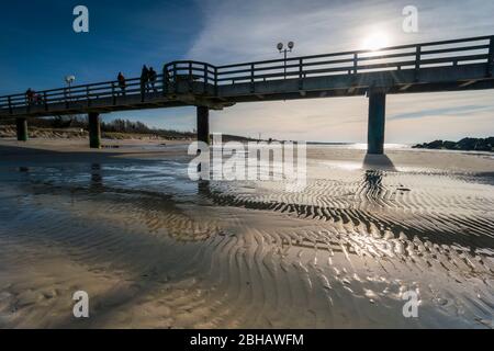 Ostsee im strahlenden Gegenlicht mit der Seebrücke in Wustrow und Spiegelung der schönen Wolken am Strand Stockfoto