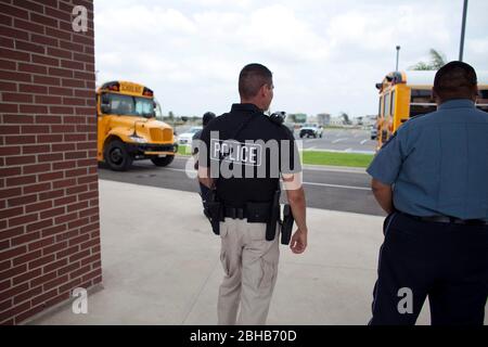 Pharr Texas USA, 13. Mai 2010: Bewaffneter Polizeibeamter beobachtet, wie Schulbusse, die mit Schülern beladen sind, die Schule für den Tag verlassen. ©Bob Daemmrich Stockfoto