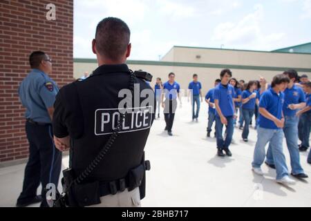 Pharr Texas USA, 13. Mai 2010: Schüler, die auf ihre Schulbusse warten, werden von der örtlichen Polizei überwacht, die an der Schule im äußersten Süden von Texas Sicherheitsdetails zugewiesen wird. Die Schüler müssen die blauen Uniformen während des Schultages tragen. ©Bob Daemmrich Stockfoto