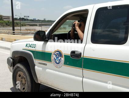 Laredo Texas USA, Juli 15 2010: Der Sicherheitsbeamte der Heimatregion blickt durch ein Fernglas, während er in seinem markierten Fahrzeug in der Nähe der Grenze zwischen den Vereinigten Staaten und Mexiko sitzt, die im Hintergrund vom Rio Grande River gekennzeichnet ist. Nach der zunehmenden Gewalt und dem Drogenhandel entlang der Grenze suchen Agenten nach Schmugglern. ©Marjorie Kamys Cotera/Bob Daemmrich Photography Stockfoto