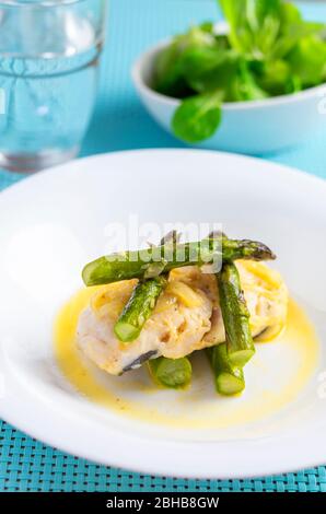 Seehechtfisch mit Zwiebeln, wildem Spargel und Fleischbrühe und Saftbeeren auf einem tiefweißen Teller, um Farben und Texturen hervorzuheben Stockfoto