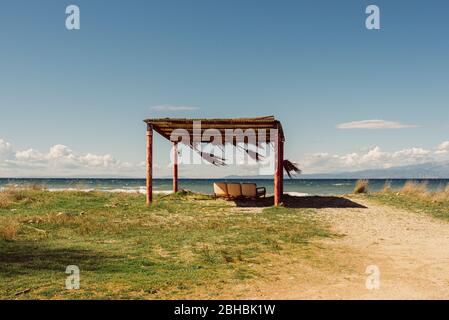 Drei leere Liegen unter rustikalem Strandzelt an einem leeren Strand in Thassos, Griechenland Stockfoto