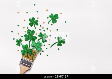 Kreatives St. Patricks Day Konzept mit Pinsel und grünen Glitzer Kleeblätter und Konfetti gemacht. Minimales flaches Lay. Stockfoto