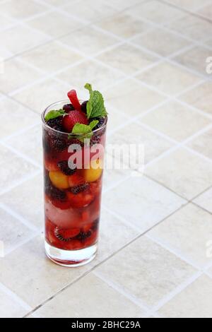 Nahaufnahme eines Glases voller bunter Früchte und Beeren und Minze, serviert mit Eis und Soda als Erfrischungsgetränk im Sommer Stockfoto