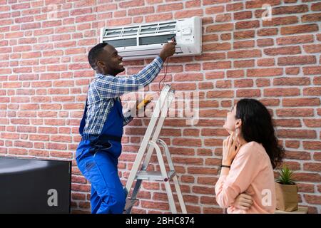 Junge Frau mit männlichen Techniker Reparatur der Klimaanlage montiert auf Wand Stockfoto