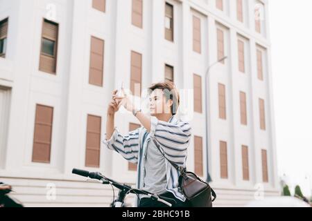 Stilvolle Menschen chatten, während Sie Handy beim Sitzen auf dem Fahrrad, im Freien. Im karierten Hemd, T-Shirt und Jeans. Close-up. Stockfoto