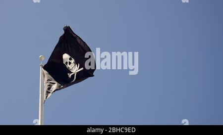 Totenkopf und Armbrone Schwarze Piratenflagge fliegen, auch bekannt als Jolly Roger, symbolisiert Gift, Tod, Gefahr und Verrat. Auf Piratenschiffen gesehen. Stockfoto