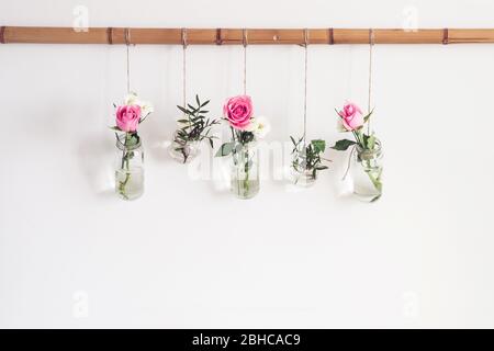 DIY stilvolle Urlaubsdekoration. Blumen in Vasen Gläser sind von der weißen Wand im Zimmer aufgehängt. Saisonale romantische Dekoration, Vorderansicht. Stockfoto