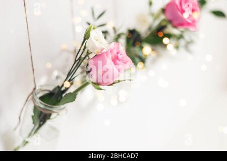Wunderschöne stilvolle Urlaubsdekoration. Blumen in Vasen Gläser sind von der weißen Wand aufgehängt. Saisonale romantische Dekoration, selektiver Fokus. Stockfoto