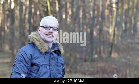 Nahaufnahme Porträt eines intelligenten Mannes mit grauen Haaren und Brille, ein Bart im warmen Winter vor dem Hintergrund des Waldes. Gegen die Stockfoto