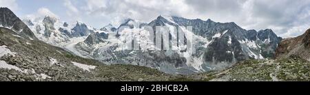 Panorama-Momentaufnahme eines Bergrückens aus schneebedeckten Felsbergen in den Schweizer Alpen, scharfe Gipfel in Wolken, graue Steine im Vordergrund Stockfoto