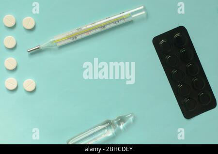 COVID-19.der Buchstabe C der Tabletten, ein Thermometer und Tablettenblase auf türkisfarbenem Hintergrund. Stockfoto