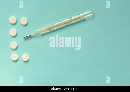COVID-19.der Buchstabe C der Tabletten und ein Thermometer auf türkisfarbenem Hintergrund. Stockfoto