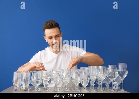 Junger Mann spielt Musik auf Gläsern mit Wasser vor farbigen Hintergrund Stockfoto