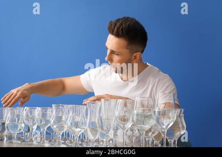 Junger Mann spielt Musik auf Gläsern mit Wasser vor farbigen Hintergrund Stockfoto
