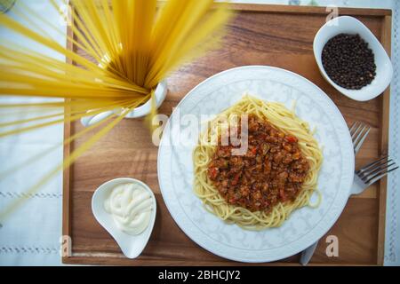Spaghetti Bolognese mit Hackfleisch, Zwiebel, gehackte Tomaten, Tomatenmark . Rohe Spaghetti-Pasta in einer Schüssel. Schwarzer Pfeffer, Mayonnaise in einer Schüssel Stockfoto