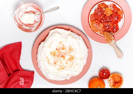 Schlagsahne und Fruchtsaft auf Baiser. Schritt für Schritt Rezept von Pavlova Kuchen mit Blutorange. Stockfoto