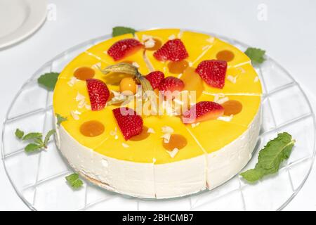 Ganze Runde in Scheiben geschnitten Orange und Vanille Diplomat Kuchen oder Torte mit Erdbeere auf der Oberseite und Obst, auf einem Glasteller einfachen Tisch. Hausgemachte französisch Rezept f Stockfoto