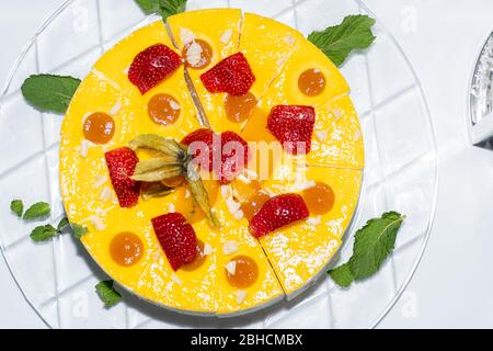 Ganze Runde in Scheiben geschnitten Orange und Vanille Diplomat Kuchen oder Torte mit Erdbeere auf der Oberseite und Obst, auf einem Glasteller einfachen Tisch. Hausgemachte französisch Rezept f Stockfoto