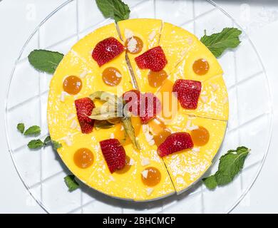 Ganze Runde in Scheiben geschnitten Orange und Vanille Diplomat Kuchen oder Torte mit Erdbeere auf der Oberseite und Obst, auf einem Glasteller einfachen Tisch. Hausgemachte französisch Rezept f Stockfoto