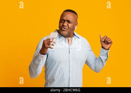 afroamerikanischer Mann mittleren Alters in Kopfhörern, der am Telefon wie ein Mikrofon singt Stockfoto