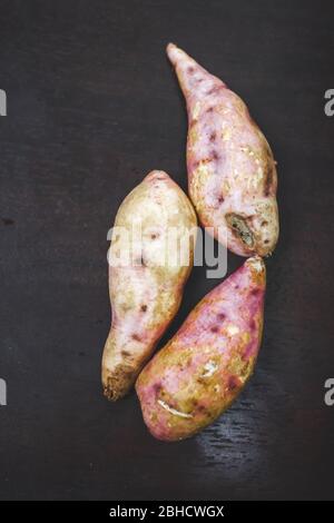 Rohe Süßkartoffeln auf Holzhintergrund Nahaufnahme. Süßkartoffel auf Holzoberfläche. Ipomoea batatas oder Shakarkandi Stockfoto