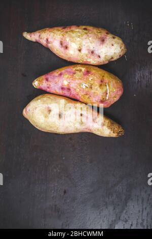 Rohe Süßkartoffeln auf Holzhintergrund Nahaufnahme. Süßkartoffel auf Holzoberfläche. Ipomoea batatas oder Shakarkandi Stockfoto