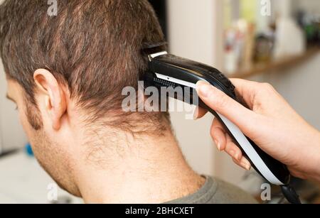 Frau macht Haarschnitt mit Haarschneider zu Mann zu Hause. Stockfoto