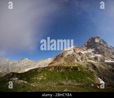 Herrliche Landschaft in der Sommernacht mit blauem Himmel und Sternen, schöne Berge mit Schnee und grünem Gras. Wunderschöner Bergrücken mit hohen felsigen Gipfeln, Touristenzelten, Wunderland. Stockfoto