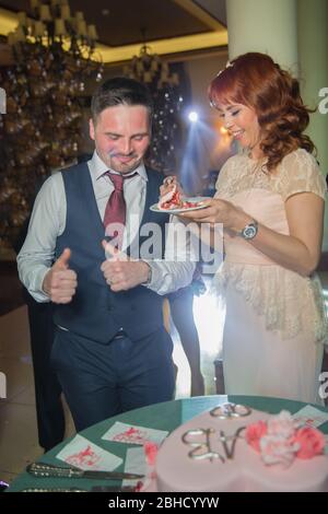 Ein unglaubliches Paar, das Hochzeitstorte isst. Schöne Brautpaar und ihr Mann essen Kuchen und sie lachen zusammen. Baku, Aserbaidschan .7.04.2019 . Stockfoto